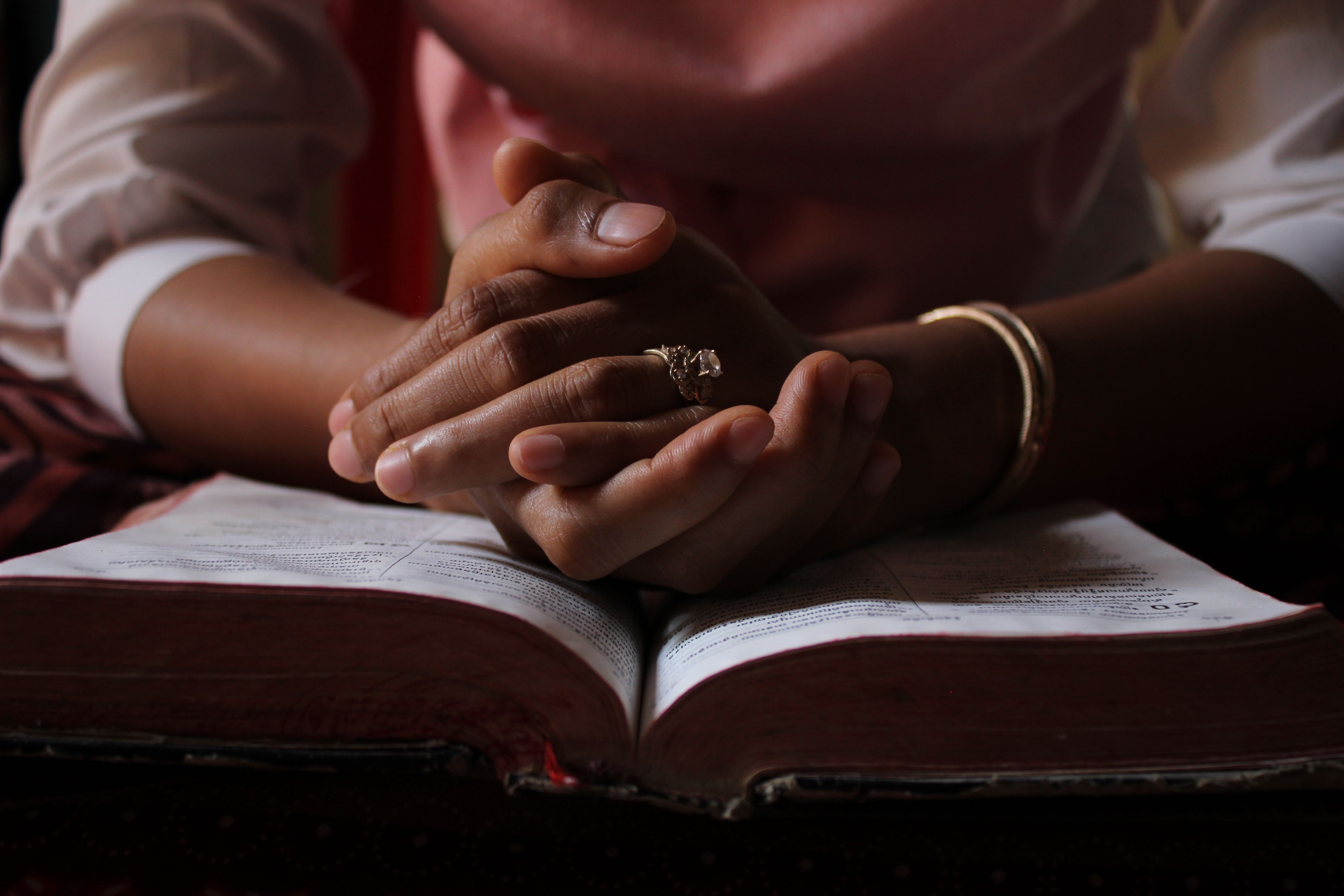 Person praying with folded hands over an open Bible for strength and healing.