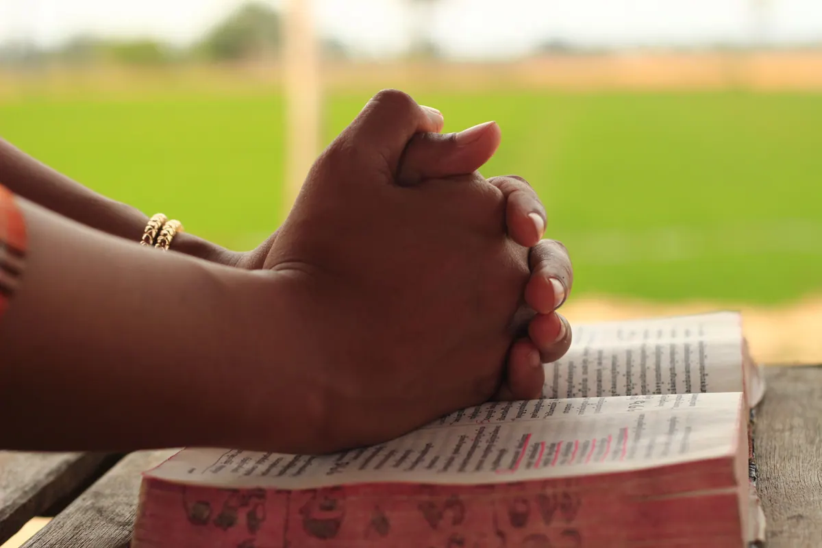Person praying over an open Bible outdoors seeking comfort