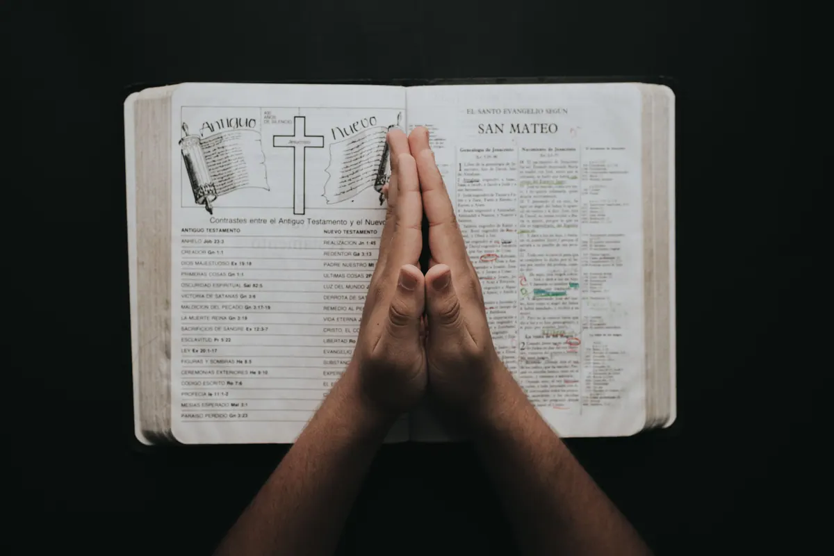 Praying hands resting on an open Bible for strength