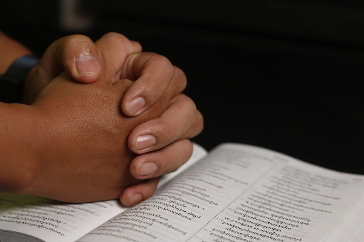 Clasped hands praying over an open Bible during a time of illness