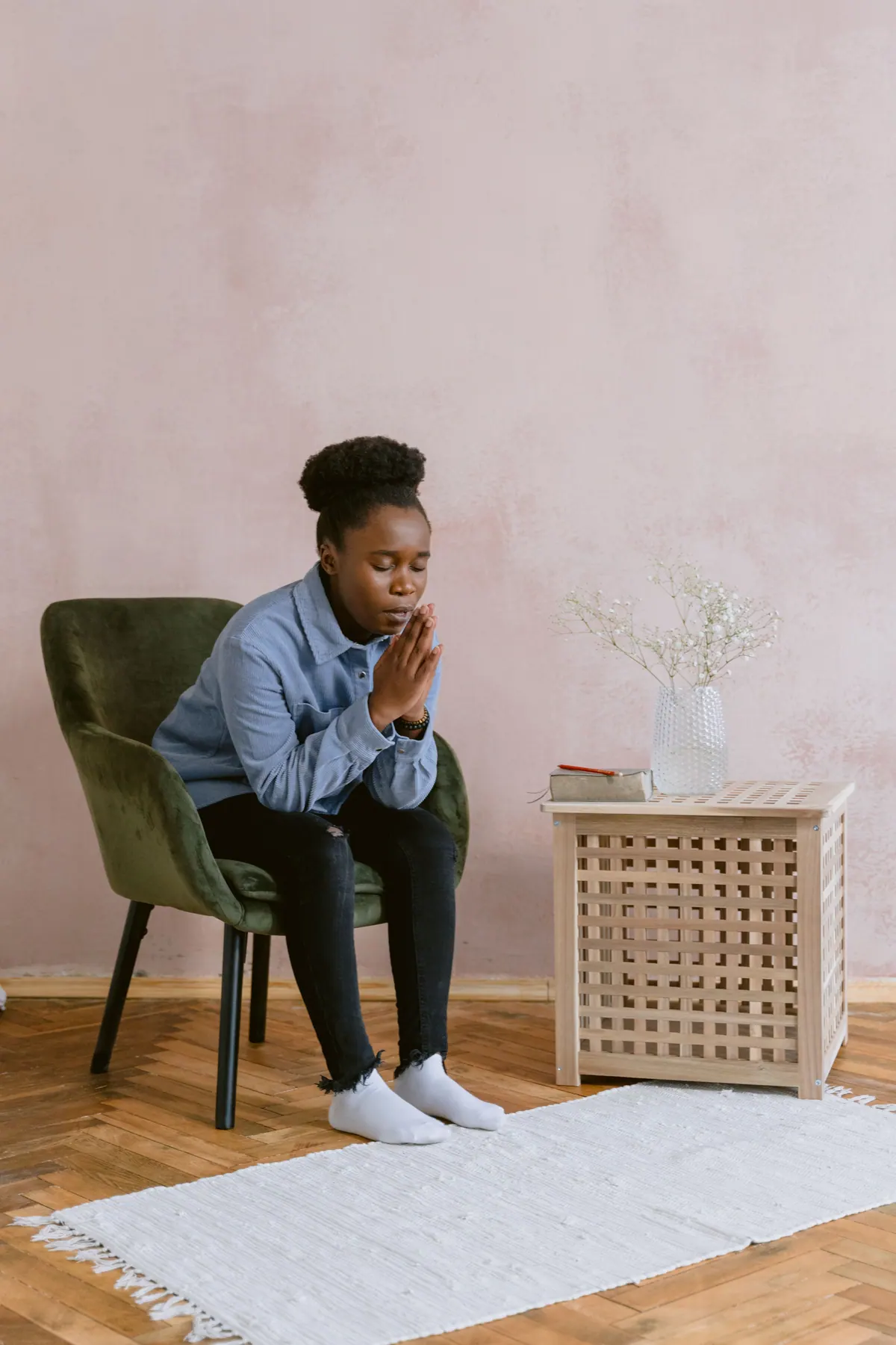 Woman seated indoors praying quietly beside a table