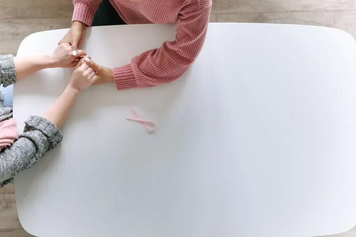 Two people holding hands near a pink cancer awareness ribbon