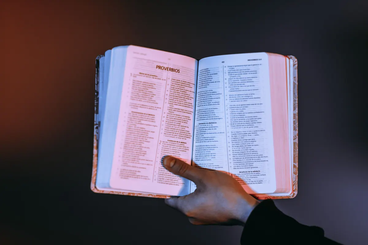 A person holding an open Bible in warm devotional light