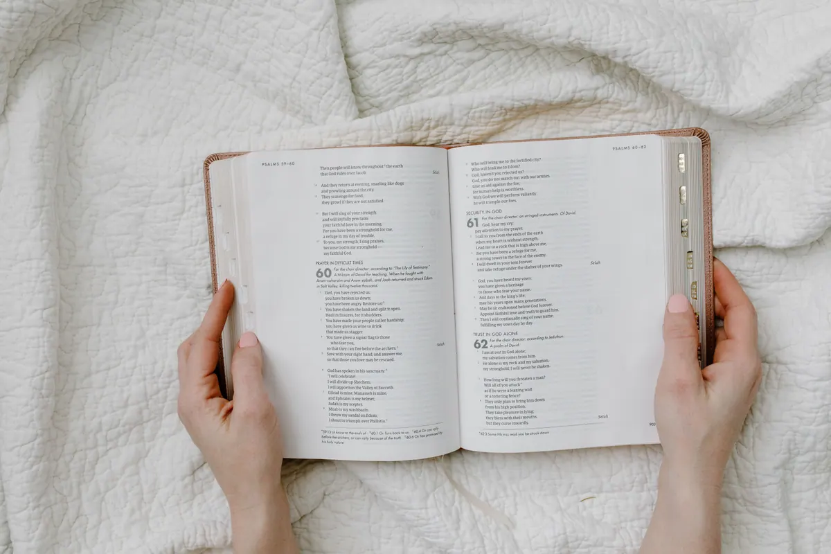 Open Bible held in hands on a white quilt for quiet prayer and reflection